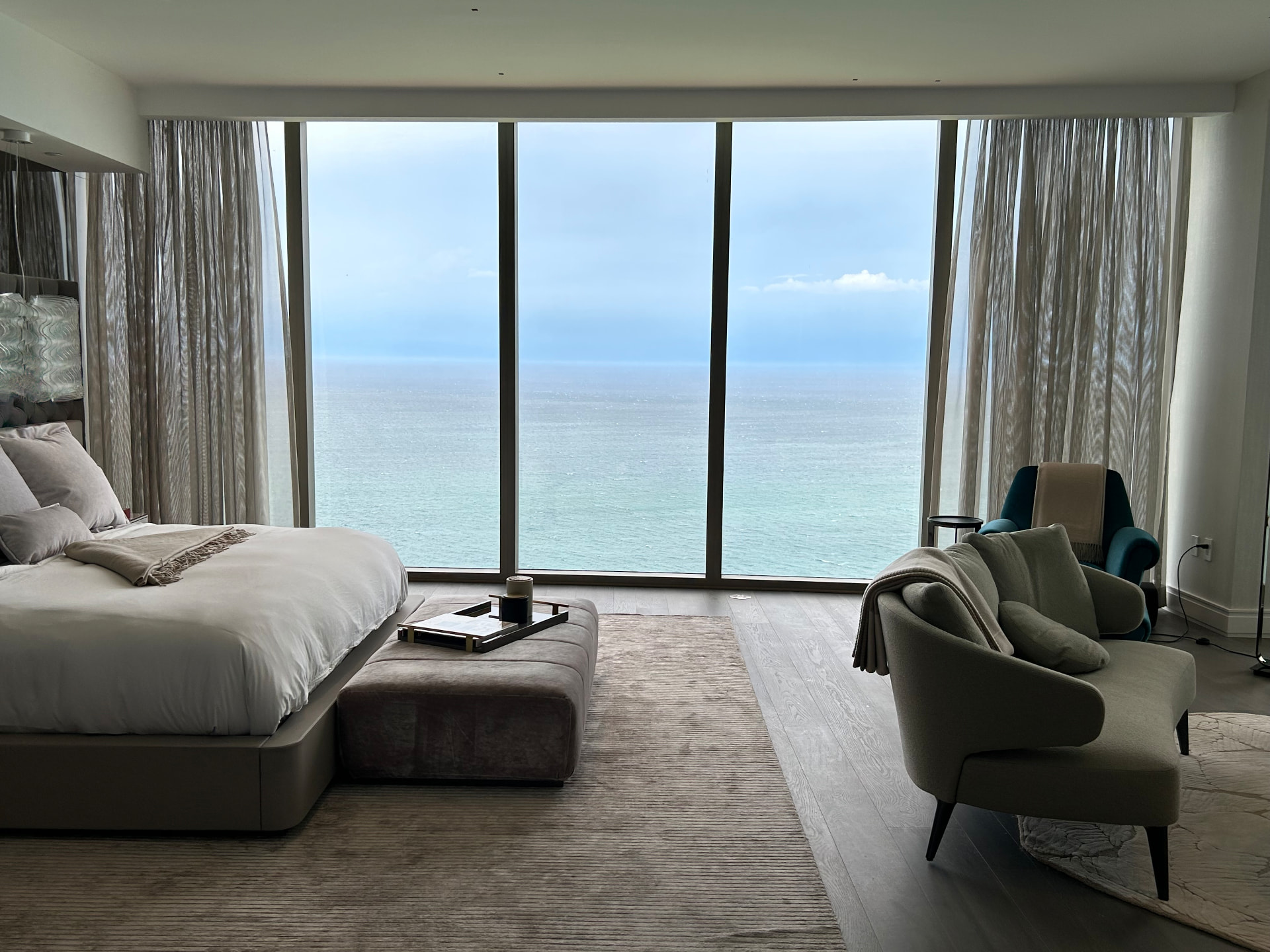 Estate at Acqualina primary bedroom with sheer drapery framing floor-to-ceiling ocean windows