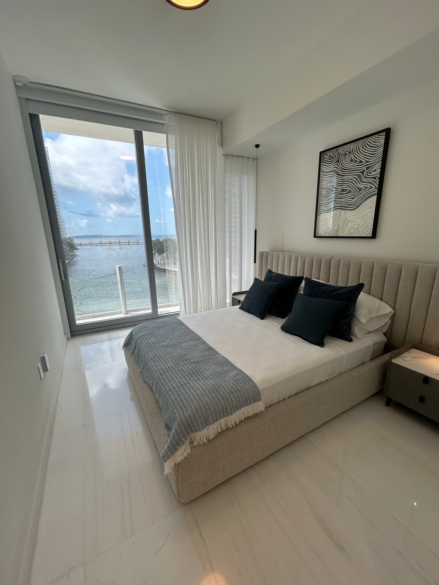 Aston Martin Residences bedroom with sheer drapery beside a bay-view slider