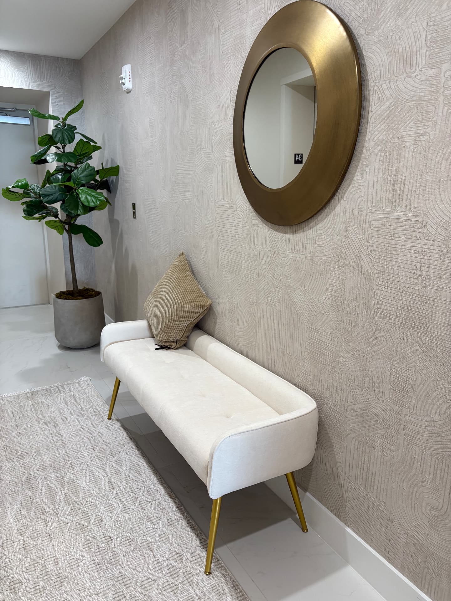 Aria Reserve entry hall with textured beige wallcovering, bench and round brass mirror